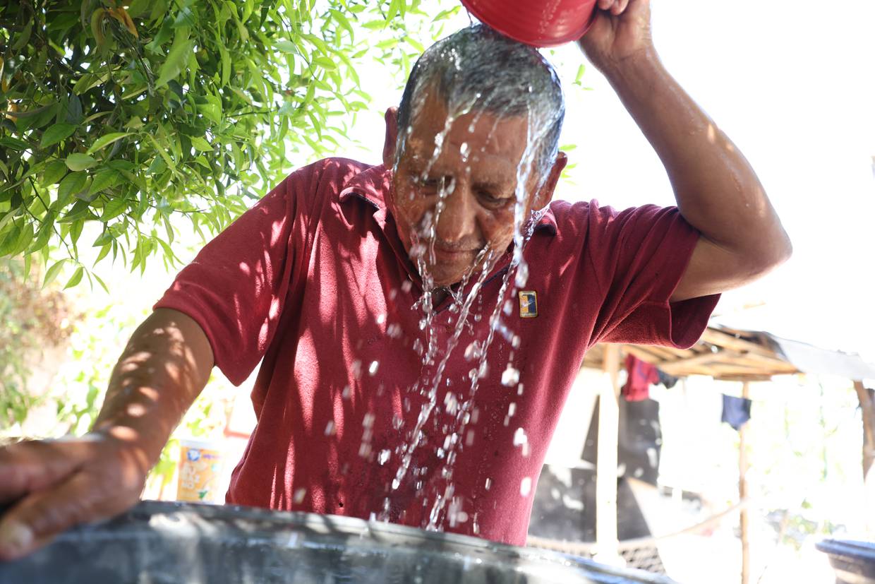 El señor don Rafael Gutiérrez Gómez de 65 años mitiga el calor echándose agua esto a la una y media de la tarde en su domicilio en la invasión Nueva Ilusión.