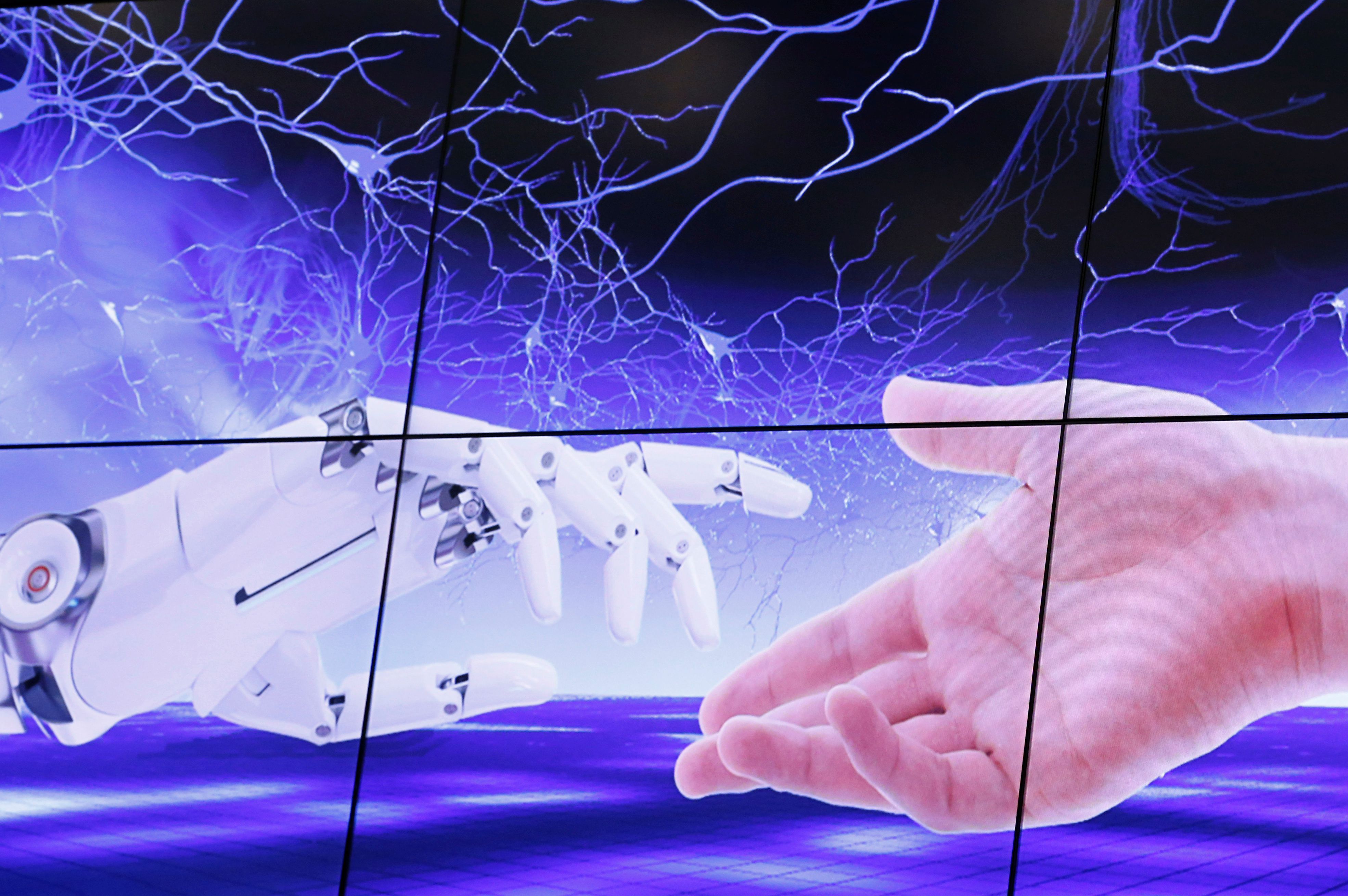 FOTO DE ARCHIVO: Una ilustración proyectada en una pantalla muestra una mano robótica y una humana moviéndose una hacia la otra durante la Cumbre Global "AI for Good" en la Unión Internacional de Telecomunicaciones (UIT) en Ginebra, Suiza, 7 de junio de 2017.    REUTERS/Denis Balibouse