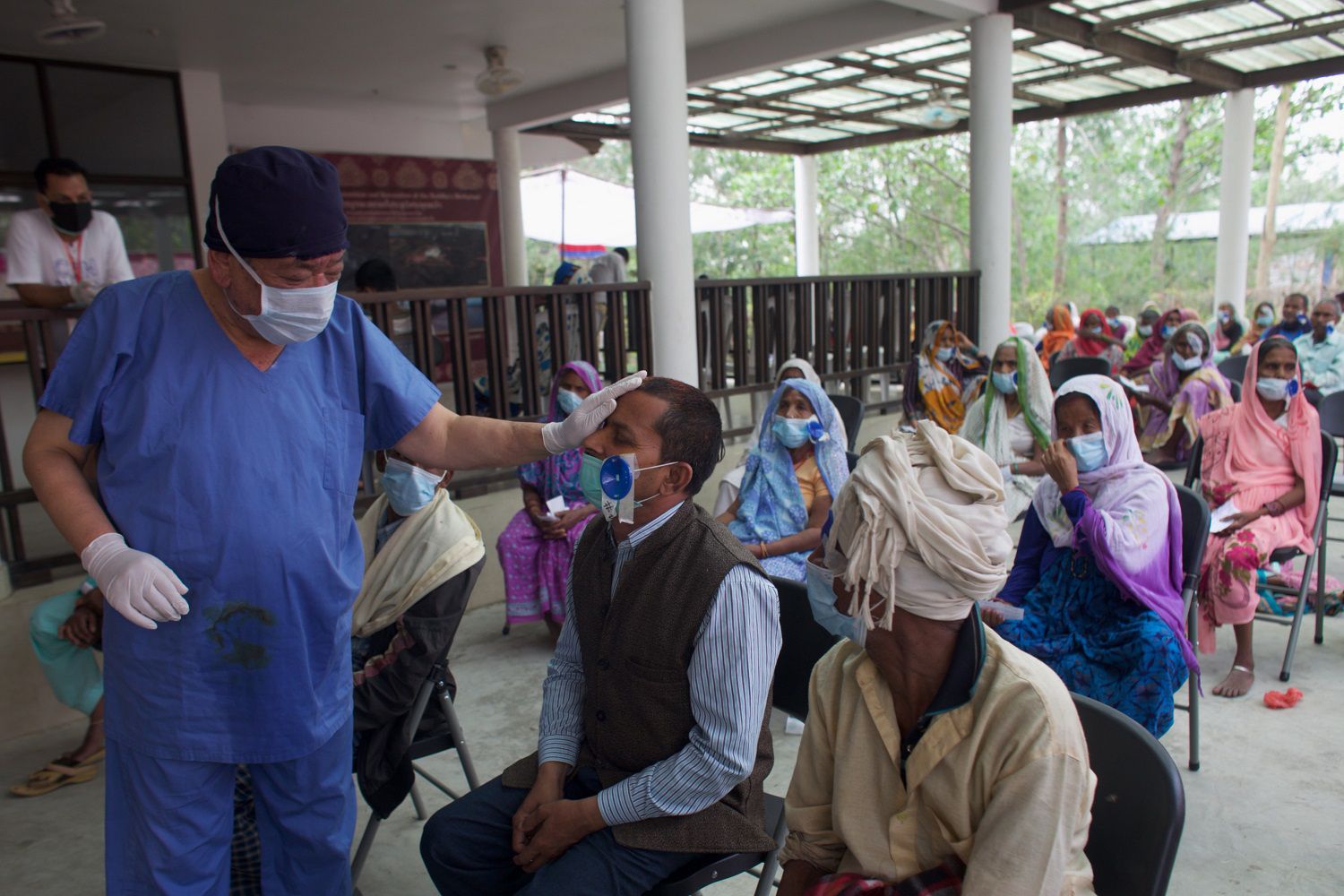 El cirujano Sanduk Ruit observa a un paciente que operó de cataratas mientras decenas más esperan ser atendidos en un hospital improvisado en Lumbini, Nepal, el 31 de mayo del 2021. (AP Photo/Bikram Rai)
