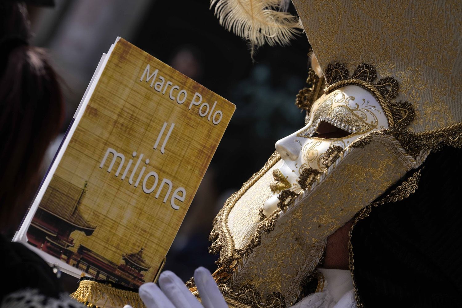 Un hombre, ataviado con una máscara, sostiene una réplica de “Los viajes de Marco Polo” ("Il milione", en italiano), que relata los viajes del explorador por Asia.