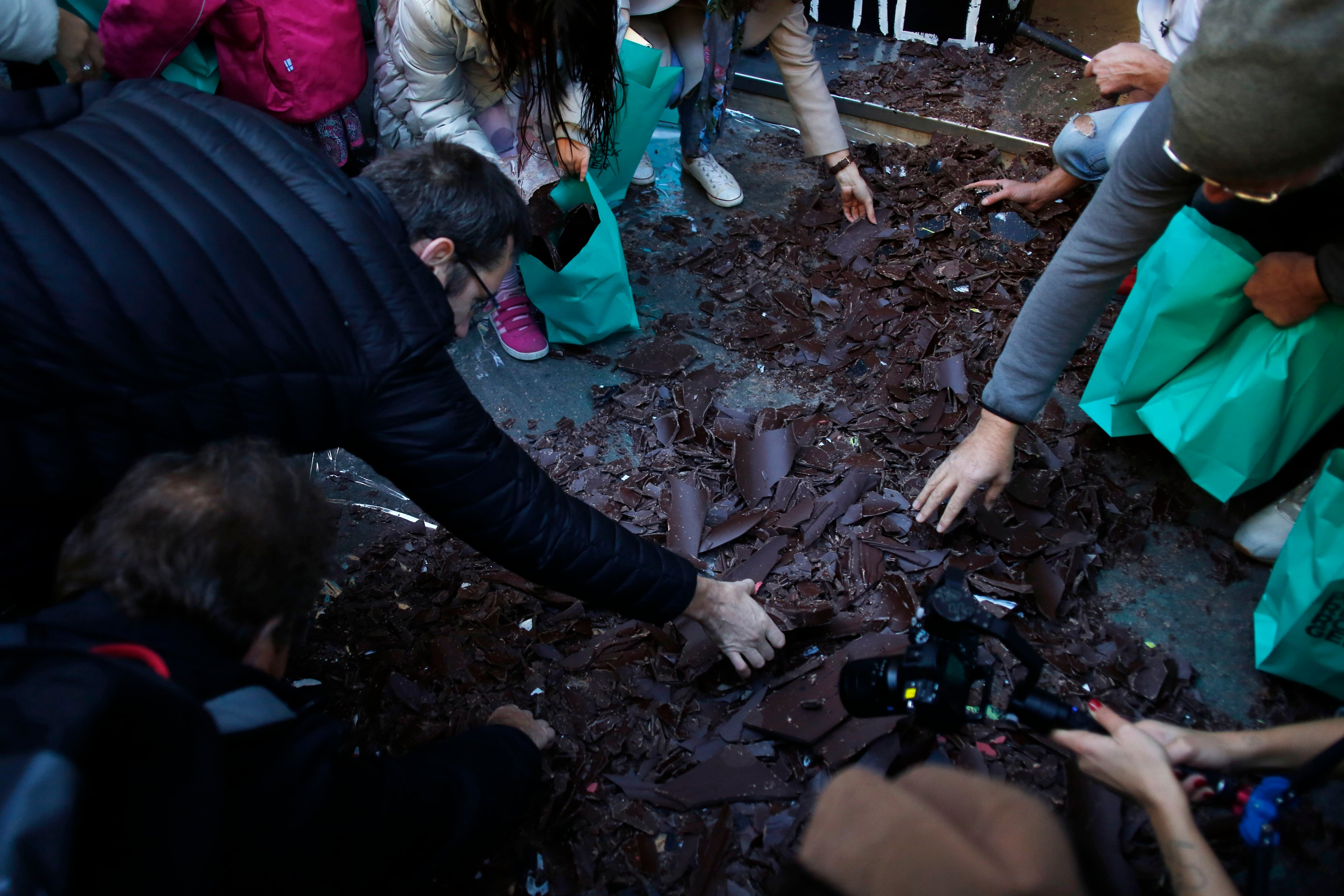 Personas recogen los trozos de una réplica hecha de chocolate del Muro de Berlín en París, el sábado 9 de noviembre de 2019. (AP Foto/Thibault Camus)