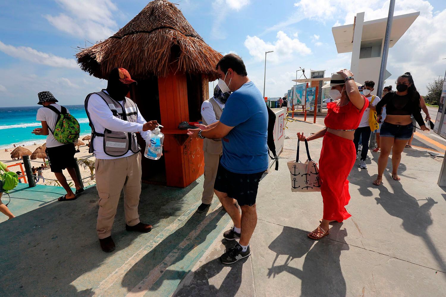 MEX3770. CANCÙN (MÉXICO), 25/01/2021.- Un hombre reparte líquido desinfectante a turistas en la playa hoy, en Cancún (México). El Gobierno de México prevé, en el mejor escenario, la llegada de 9,22 millones de turistas a hoteles, una ocupación hotelera del 66,5 % e ingresos en centros de hospedaje por 1.065 millones de dólares en el invierno de 2021, la última temporada de este año. EFE/Alonso Cupul
