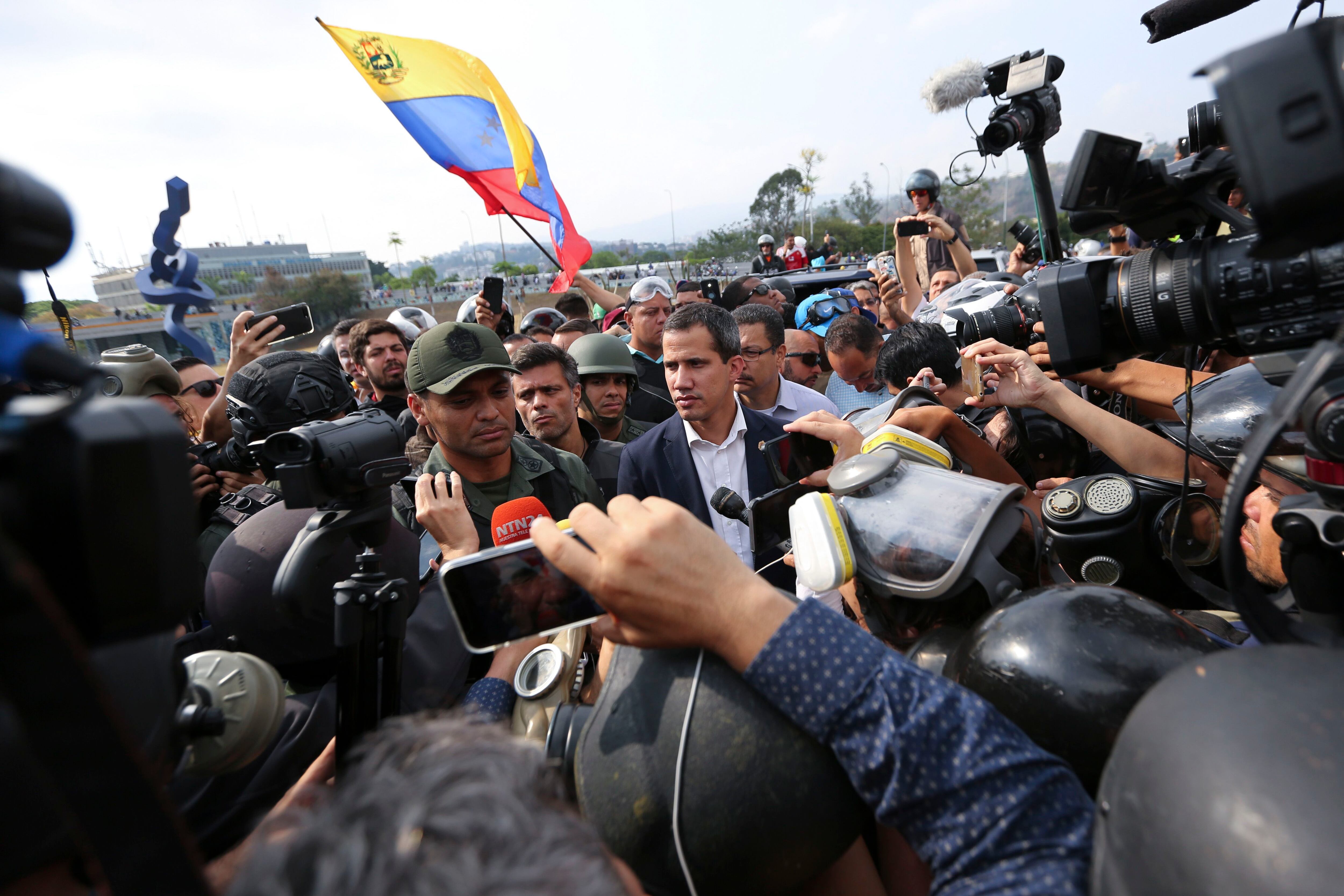 Venezuela's opposition leader and self-proclaimed president Juan Guaido, center, stands with an unidentified military officer who is helping to lead a military uprising, center left, as they talk to the press and supporters outside La Carlota air base in Caracas, Venezuela, Tuesday, April 30, 2019. Guaidó took to the streets with activist Leopoldo Lopez and a small contingent of heavily armed troops early Tuesday in a bold and risky call for the military to rise up and oust Maduro. (AP Photo/Fernando Llano)