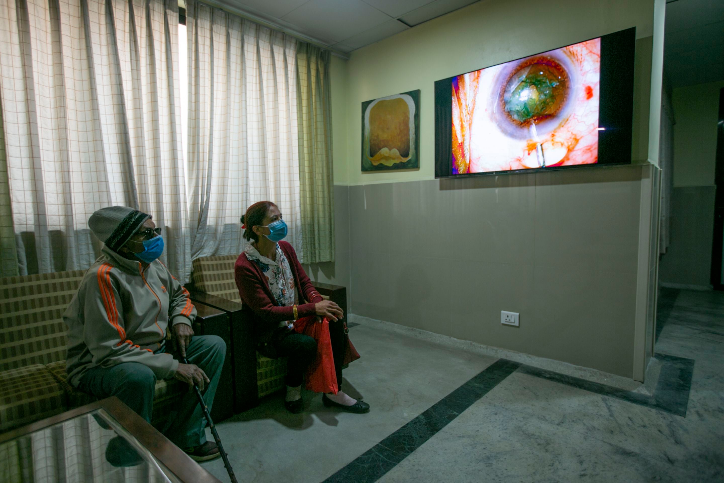 Una pacienta de edad avanzada (izq) y su acompañante observan la transmisión en vivo de una operación de cataratas realizada por el doctor Sanduk Ruit en un hospital de Katmandú, Nepal, el 26 de marzo del 2021. (AP Photo/Niranjan Shrestha)