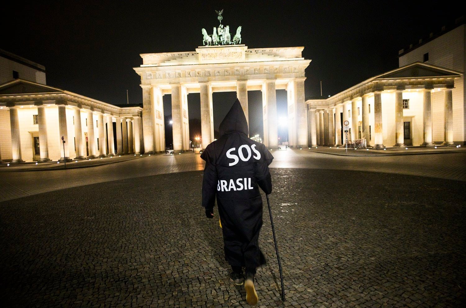 El activista y artista brasileño Rafael Puetter, disfrazado de la Parca, camina frente a la Puerta de Brandeburgo en una protesta solitaria la madrugada del miércoles 7 de abril de 2021. (AP Foto/Markus Schreiber)