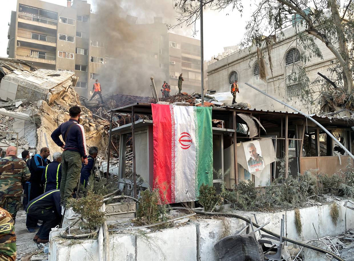 Una bandera iraní cuelga mientras el humo se eleva después de lo que medios de comunicación iraníes dijeron que fue un ataque israelí contra un edificio cerca de la embajada iraní en Damasco, Siria 1 de abril 2024. REUTERS/Firas Makdesi