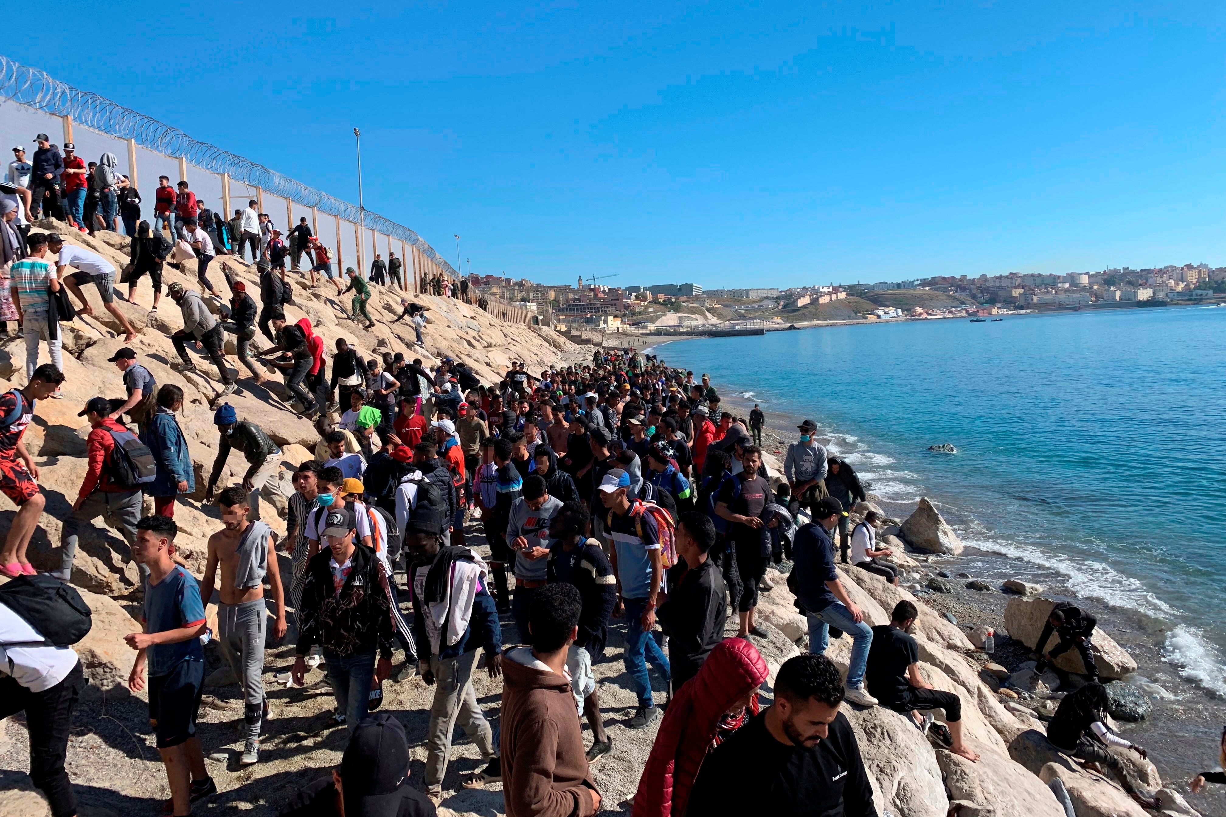 Un grupo de personas tratan de cruzar la valla fronteriza que separa Fnideq (Castillejos, Marruecos) y Ceuta este miércoles, tras la llegada de hasta 8.000 inmigrantes a Ceuta y Melilla en los dos últimos días. EFE/ Mohamed Siali
