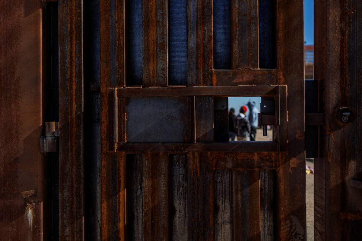FOTO DE ARCHIVO: Migrantes que buscan asilo en EEUU vistos a través de una pequeña abertura en la valla fronteriza junto al río Bravo, la frontera entre México y EEUU, visto desde El Paso, Texas, EEUU, 22 de diciembre, 2022. REUTERS/Carlos Barria