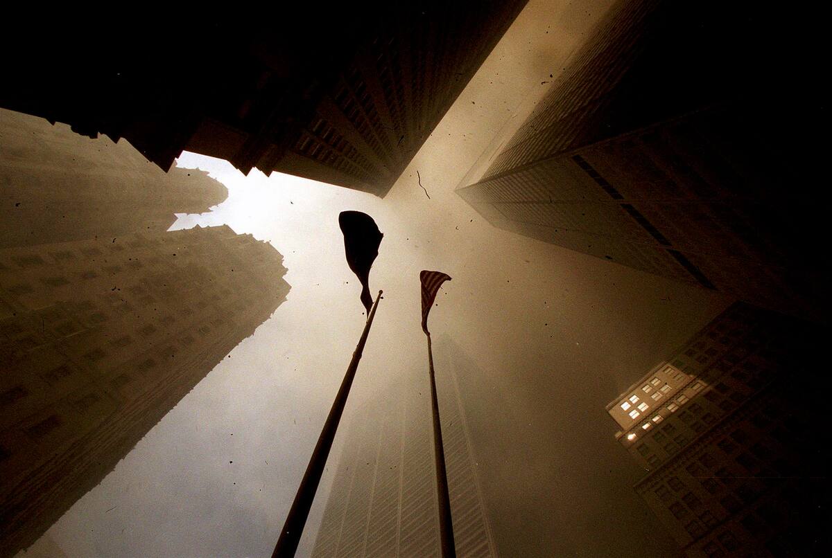 As the sun peaks through heavy smoke, two flags wave as debris continues to fall following the attack and collapse of the World Trade Towers in lower Manhattan on September 11, 2001.