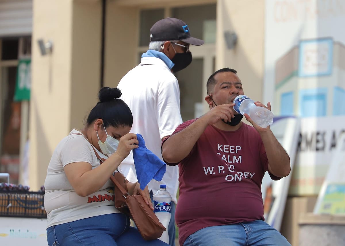 Un hombre bebe agua mientras espera el camión para mitigar el intenso calor y no deshidratarse.