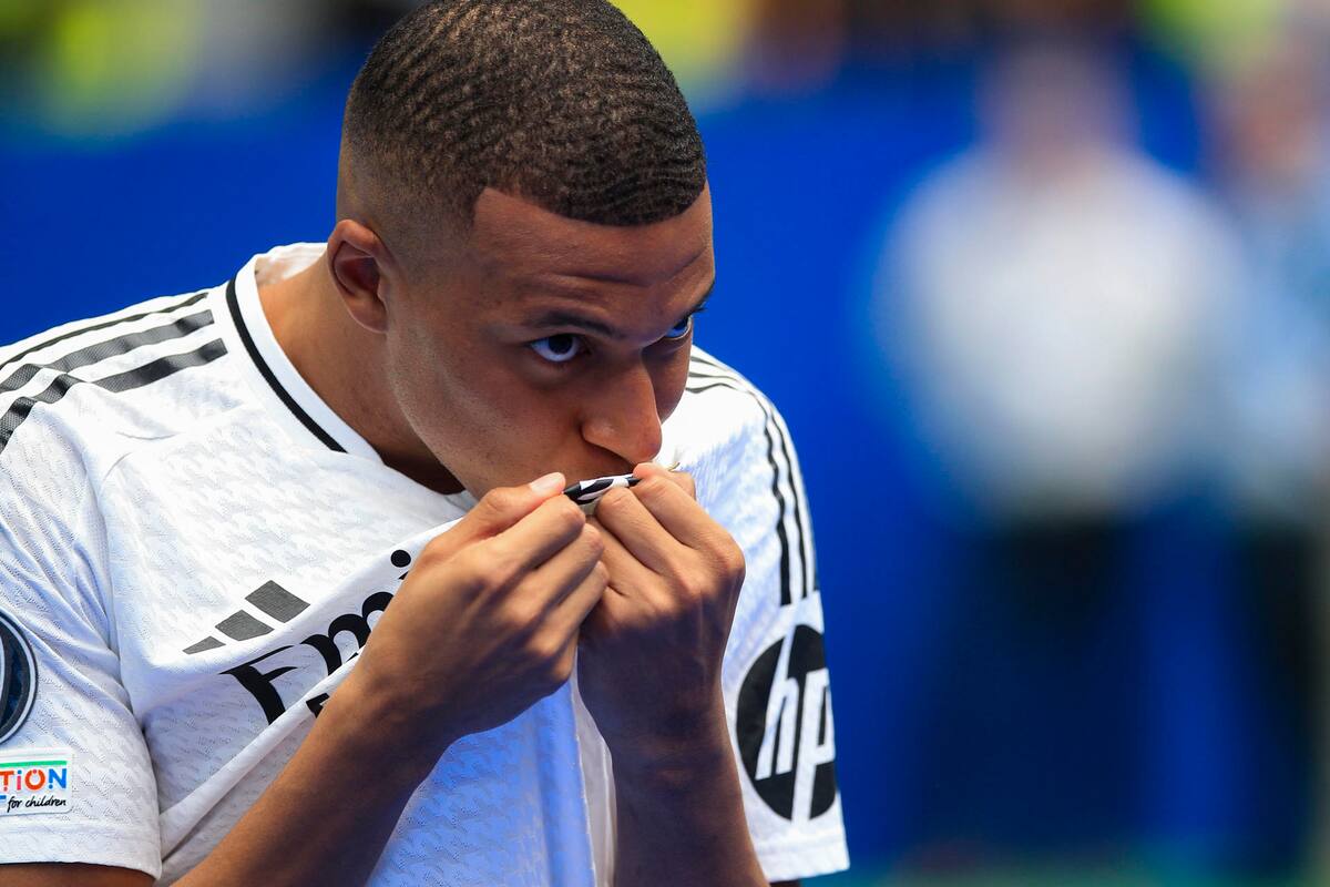 El francés Kylian Mbappé besa el escudo del Real Madrid durante su presentación como nuevo jugador del club, este martes en el estadio Santiago Bernabéu de Madrid. Mbappé firmó este martes el contrato que le une al conjunto blanco para las próximas cinco temporadas. EFE/Chema Moya