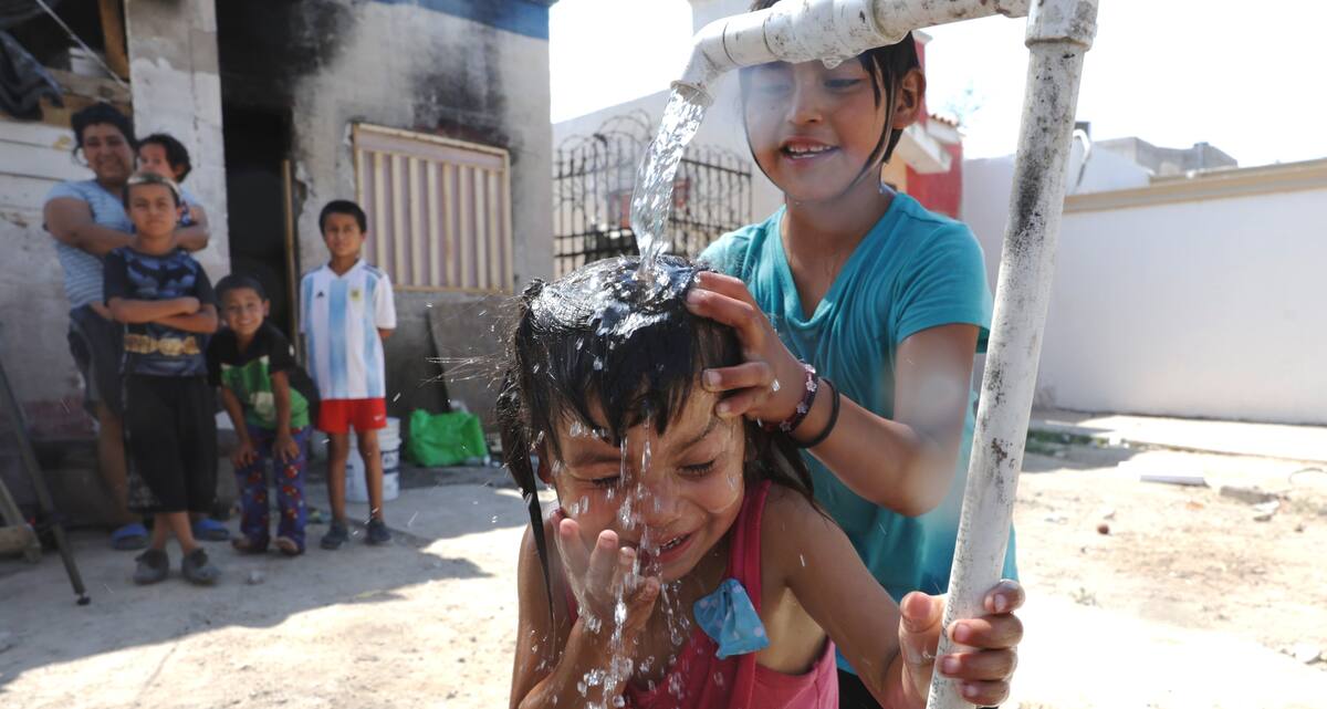 Dos niños integrantes de la familia Vázquez Tapia mitigan el calor con el pequeño chorro de la llave, en la vivienda que habitan en el fraccionamiento Villa Verde. FOTO: TEODORO BORBÓN
