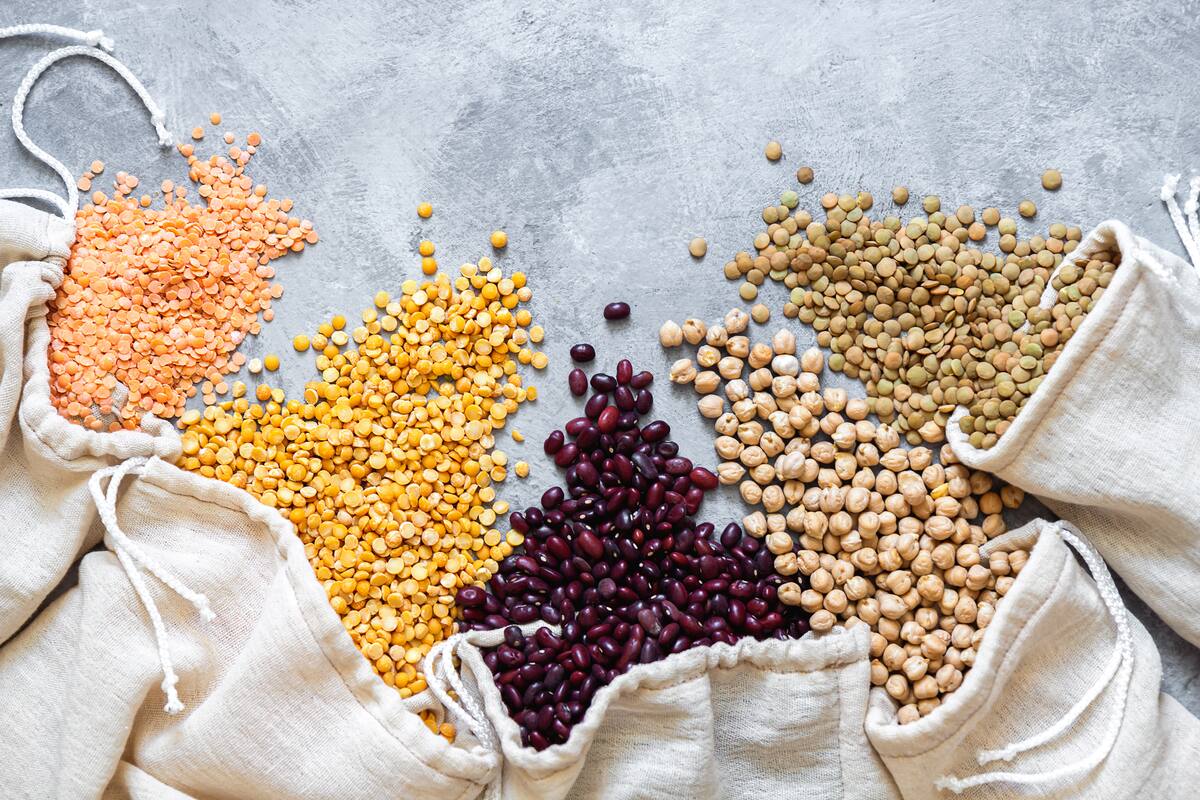 Various legumes in eco bags. Lentils, beans, peas, chickpeas are scattered on a gray background. Flat lay with place for text.