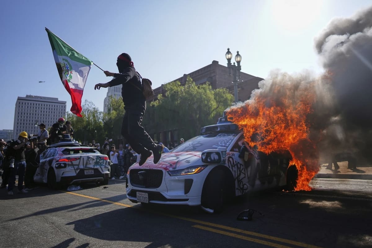 Un manifestante salta de un taxi Waymo en llamas cerca del Centro de Detención Metropolitano en el centro de Los Ángeles, el domingo 8 de junio de 2025, tras la redada de inmigración de anoche. | Crédito: AP/Eric Thayer.