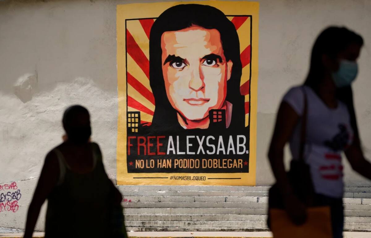 ARCHIVO – Varios peatones caminan frente a un cartel que pide la liberación del empresario colombiano y enviado especial de Venezuela Alex Saab, en Caracas, Venezuela, el 9 de septiembre de 2021. (AP Foto/Ariana Cubillos, Archivo)