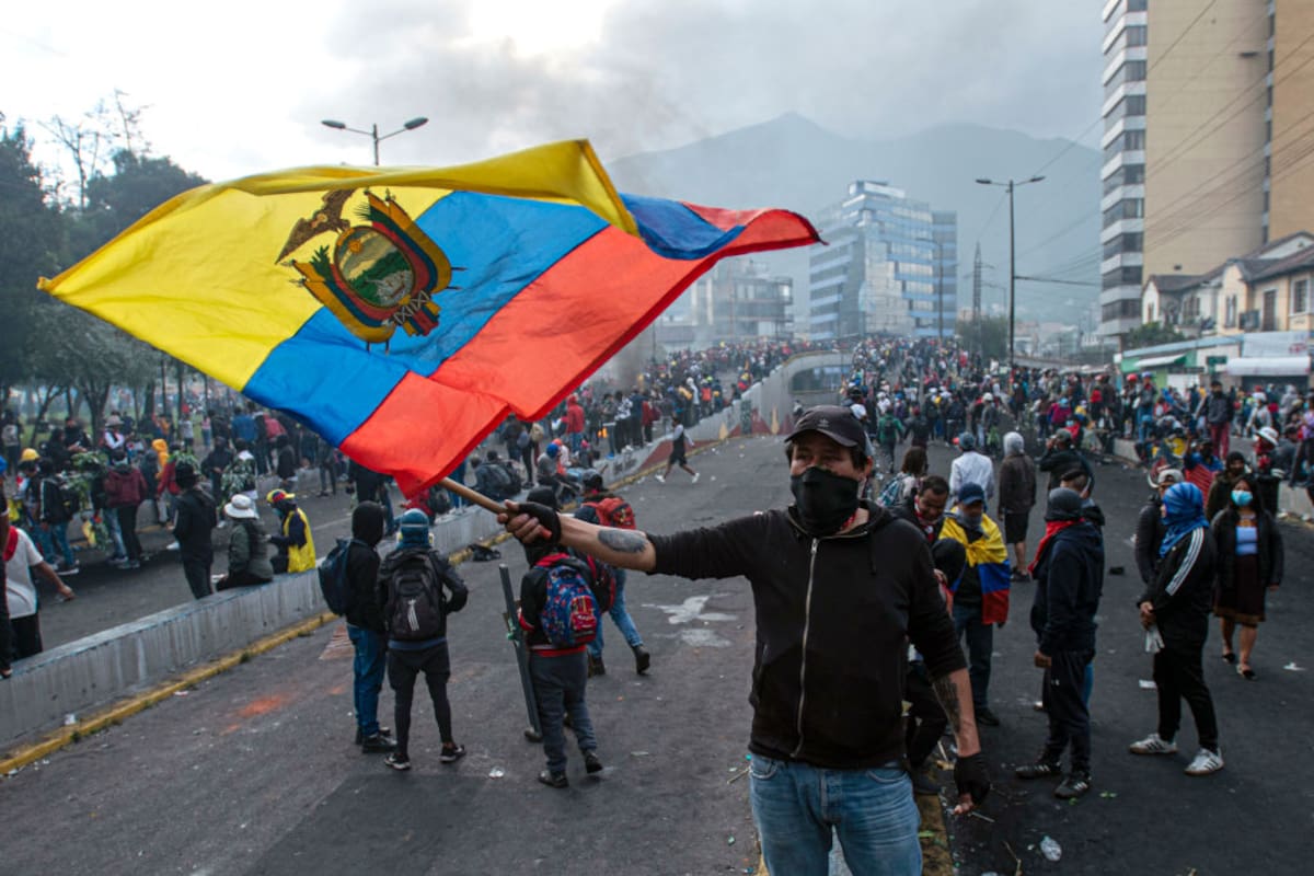 QUITO, ECUADOR - JUNE 22: A masked demonstrator waves a flag of Ecuador during the tenth day of protests against president Guillermo Lasso on June 22, 2022 in Quito, Ecuador. Protesters demand social and economic reforms amid rising inflation, unemployment, poverty and inequality. (Photo by Klaus Galiano/Agencia Press South/Getty Images)