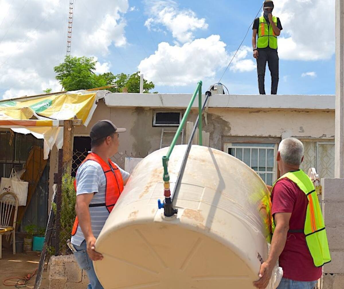 Dos personas cargan un tinaco para colocarlo en el techo de una casa. FOTO: BANCO DIGITAL