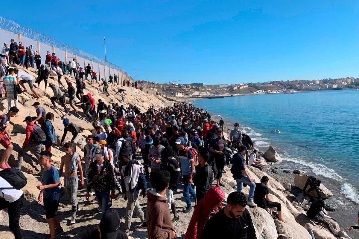 Un grupo de personas tratan de cruzar la valla fronteriza que separa Fnideq (Castillejos, Marruecos) y Ceuta este miércoles, tras la llegada de hasta 8.000 inmigrantes a Ceuta y Melilla en los dos últimos días. EFE/ Mohamed Siali