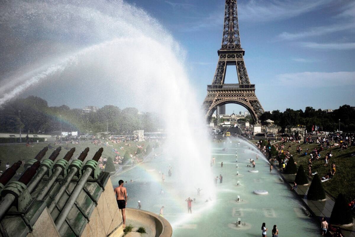 Unas personas se refrescan en las fuentes de los Jardines del Trocadero, frente a la Torre Eiffel, en París, el viernes 28 de junio de 2019. (AP Foto/Lewis Joly)