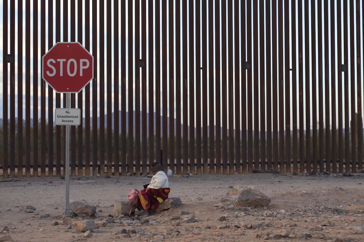 -FOTODELDÍA- EA2163. LUKEVILLE (ESTADOS UNIDOS), 12/12/2023.- Una mujer intenta mantenerse caliente mientras espera a lo largo del muro fronterizo estadounidense para ser procesada por la Patrulla Fronteriza estadounidense hoy, en Lukeville, Arizona (EE.UU.). El aumento del flujo de migrantes en la frontera de Arizona con México provocó una ola de llamados al presidente de Estados Unidos, Joe Biden, por parte de políticos y funcionarios, inclusive varios demócratas, para que envíe soldados y recursos con el fin de restaurar la normalidad en el estado, que mantiene cerrado uno de sus puertos fronterizos más importantes. EFE/ Allison Dinner