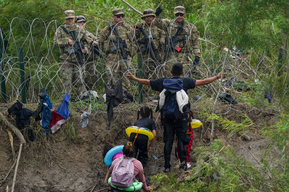 Un migrante interpela a uniformados de la Guardia Nacional de Texas al otro lado de una barrera de púas metálica en el Río Bravo, visto desde Matamoros, México, el 11 de mayo de 2023. (AP Foto/Fernando Llano)