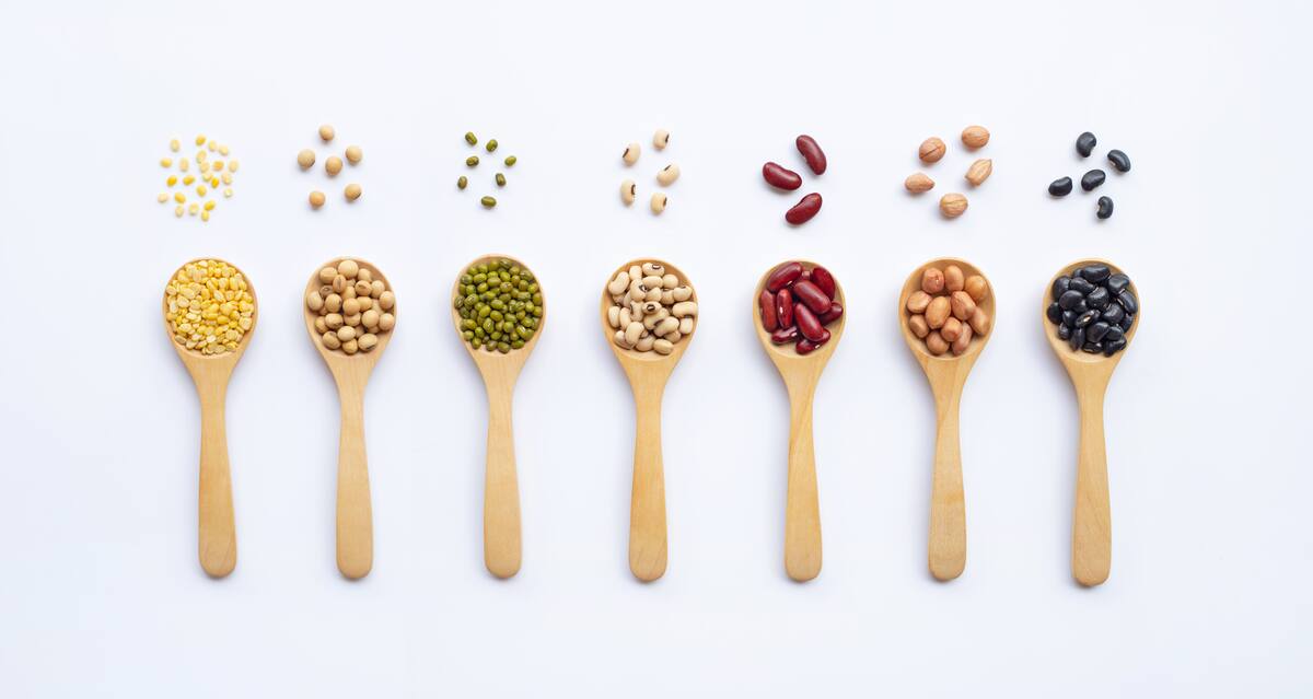 Different types of legumes on wooden spoon, white background.