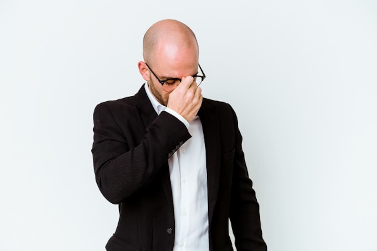 Young business caucasian bald man isolated on blue background having a head ache, touching front of the face.