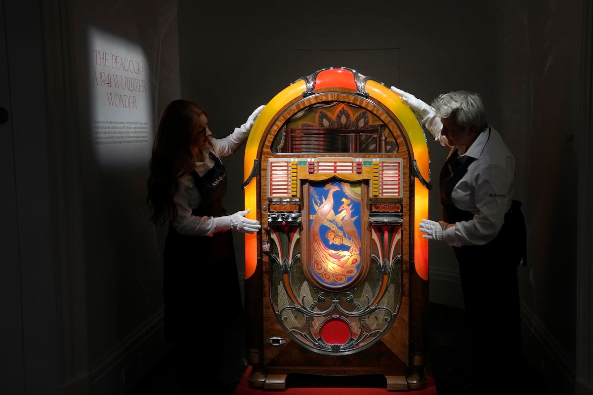 Empleados de Sotheby's colocan una rocola de diseño 'Peacock' Wurlitzer Modelo 850 de Paul Fuller, estadounidense, de cerca de 1941, en las salas de subastas de Sotheby's en Londres, el jueves 3 de agosto de 2023. Más de 1.400 artículos personales de Freddie Mercury, incluidos sus extravagantes vestuarios, borradores escritos a mano de "Bohemian Rhapsody" y el piano de media cola que usó para componer grandes éxitos de Queen, se exhibirán en la casa de subastas Sotheby's Londres antes de su venta. (Foto AP/Kirsty Wigglesworth)