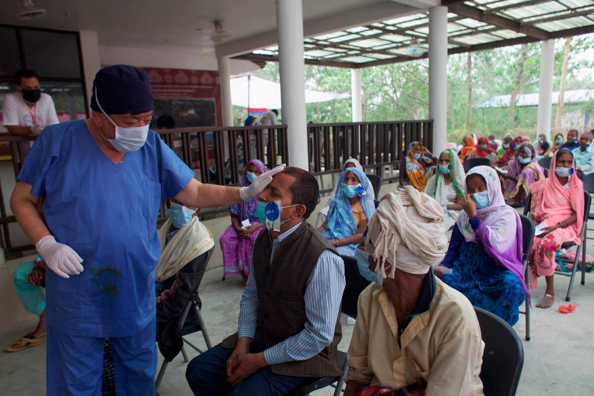 El cirujano Sanduk Ruit observa a un paciente que operó de cataratas mientras decenas más esperan ser atendidos en un hospital improvisado en Lumbini, Nepal, el 31 de mayo del 2021. (AP Photo/Bikram Rai)