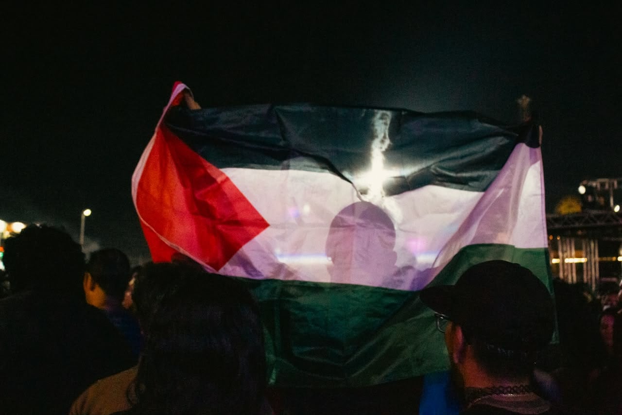 Una bandera de Palestina se alzó entre el público durante la presentación de Inspector en las Fiestas del Sol 2026, mientras asistentes participaban en el slam. Foto: René Acosta.