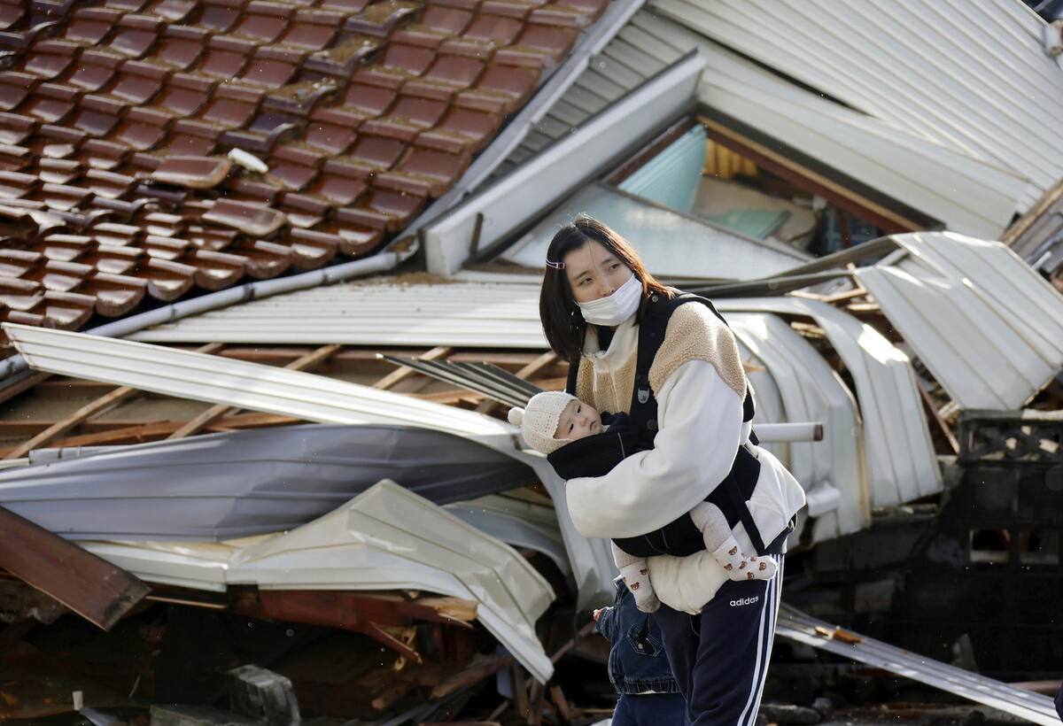 Una mujer, con un bebé en brazos, delante de casas derribadas por sismos y tsunami en Suzu, en la prefectura de Ishikawa, Japón, el 4 de enero de 2024. (Kyodo News vía AP)