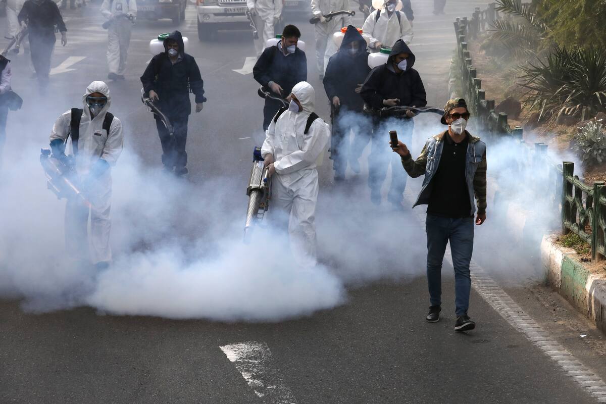 Fotografía del 13 de marzo de 2020 de bomberos desinfectando una plaza mientras un hombre graba video en Teherán, Irán. (AP Foto/Vahid Salemi)