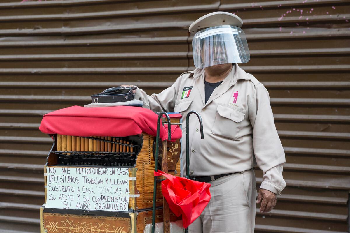 Un organillero que porta una careta protectora contra el coronavirus pide cooperación a transeúntes el sábado 16 de mayo de 2020, en la Ciudad de México. (AP Foto/Christian Palma)