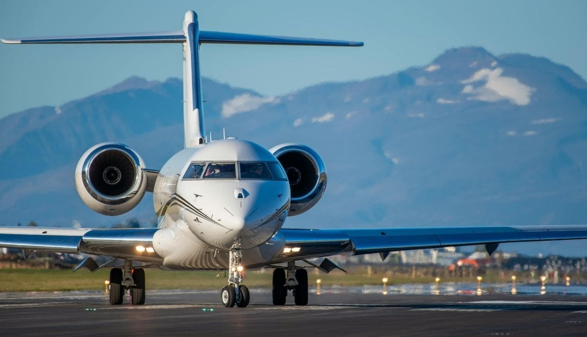 Vista frontal de un jet privado de lujo operando en una pista de aterrizaje bajo un cielo claro y con montañas al fondo. | Canva