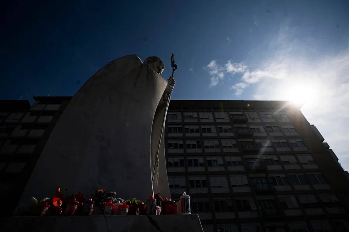 Velas y flores a los pies de la estatua de Juan Pablo II en la entrada del hospital Gemelli de Roma. / EFE