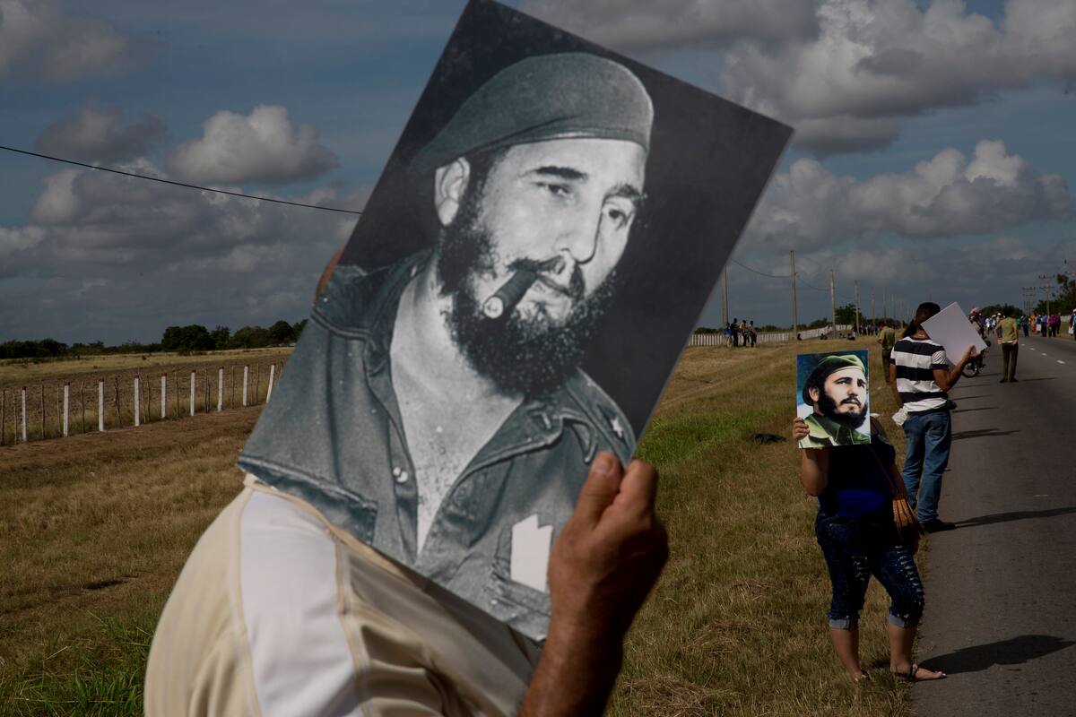 FILE - In this Dec. 2, 2016 file photo, a man uses an image of Fidel Castro to shade himself from the sun while waiting for the convoy carrying the ashes of Cuba's late leader, along the central road near Yarigua, Las Tunas, Cuba. The convoy traced in reverse the victory tour Castro and his bearded rebels took after overthrowing the forces of strongman Fulgencio Batista in 1959, to his final resting place in the eastern city of Santiago. (AP Photo/Rodrigo Abd, File)