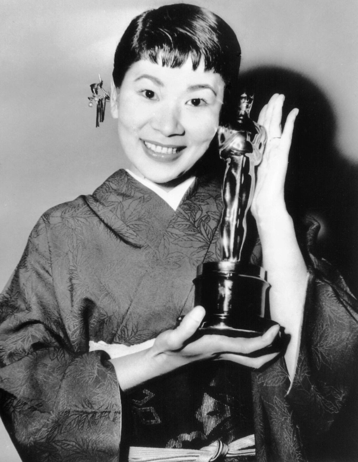ARCHIVO – La actriz japonesa Miyoshi Umeki posa con el Premio de la Academia a mejor actriz de reparto por su papel en "Sayonara", mientras el presentador Anthony Quinn la mira en los Premios de la Academia en Los Angeles el 26 de marzo de 1958. Umeki es la primera persona de Japón en ganar un Oscar. (Foto AP)
