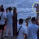 Hombre interrumpe la foto de boda de una pareja en la playa saliendo del mar en traje de baño