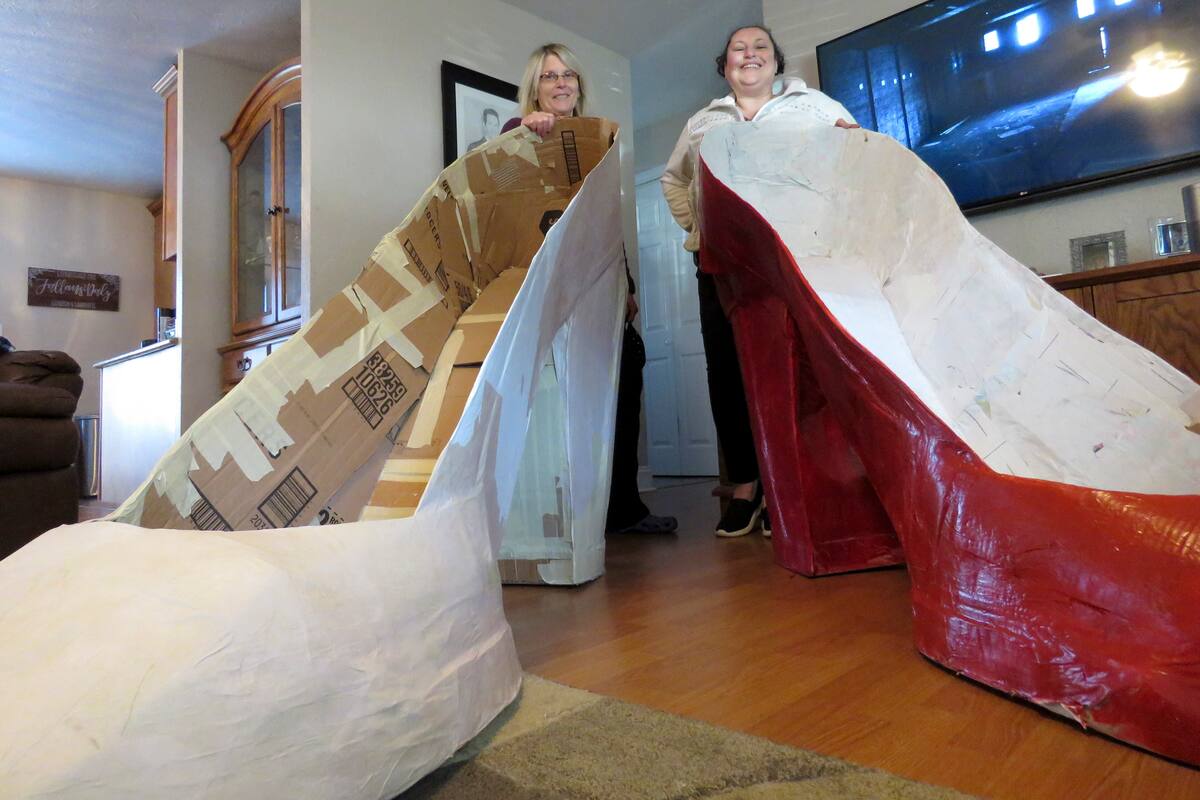 Charlotte "Charlie" Jallans-Daly, derecha, y su esposa, Sharon Jallans-Daly, posan tras un par de zapatillas enormes, parte de las decoraciones para su "casa-carroza" inspirada en "El mago de Oz", el miércoles 13 de enero del 2021 en Nueva Orleans. Con la cancelación de los tradicionales desfiles de Mardi Gras debido a la pandemia de coronavirus, miles alrededor de la ciudad han decorado sus casas para celebrar el Carnaval. (AP Foto/Janet McConnaughey)
