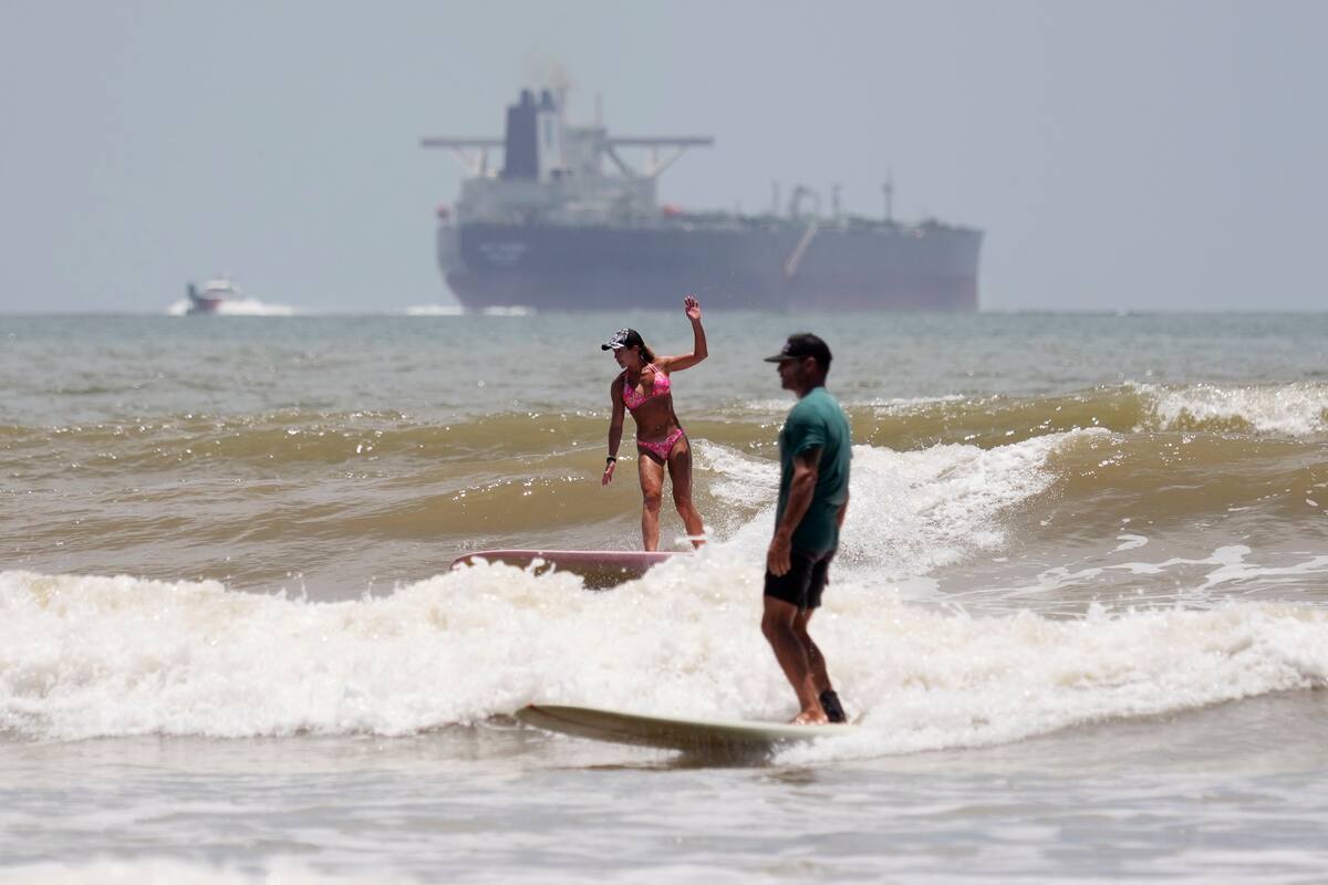 Un barco petrolero se dirige a aguas abiertas mientras los surfistas aprovechan las olas ante la llegada del huracán Beryl en Port Aransas, Texas, el sábado 6 de julio de 2024. (AP Foto/Eric Gay)