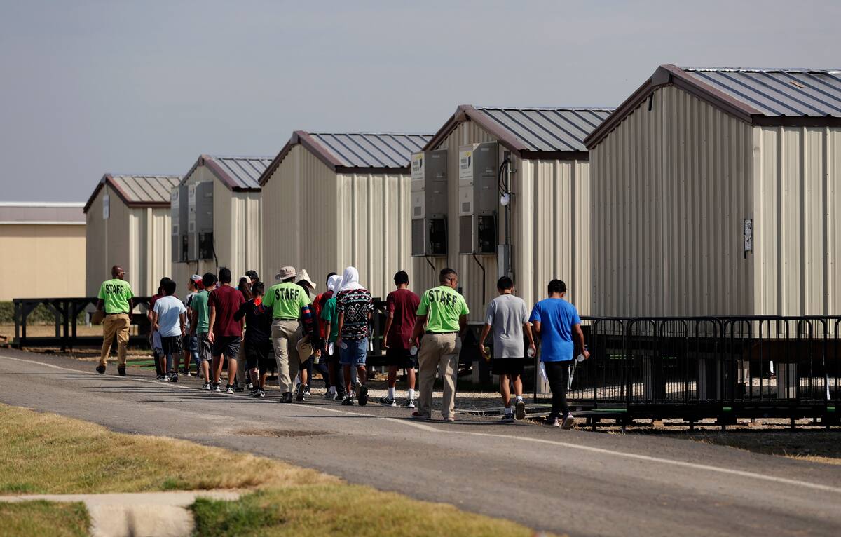 Personal del nuevo centro de detención de migrantes menores de edad de Carrizo Springs, Texas, acompaña a algunos jóvenes a las estructuras rodantes que funcionan como habitaciones. (AP Foto/Eric Gay)