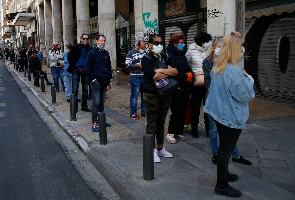 Decenas de personas haciendo cola para entrar a una carnicería en Atenas el 17 de abril del 2020. El uso de tapabocas por el coronavirus elimina una cantidad de gestos faciales que facilitan las comunicaciones entre las personas. (AP Photo/Lefteris Pitarakis)