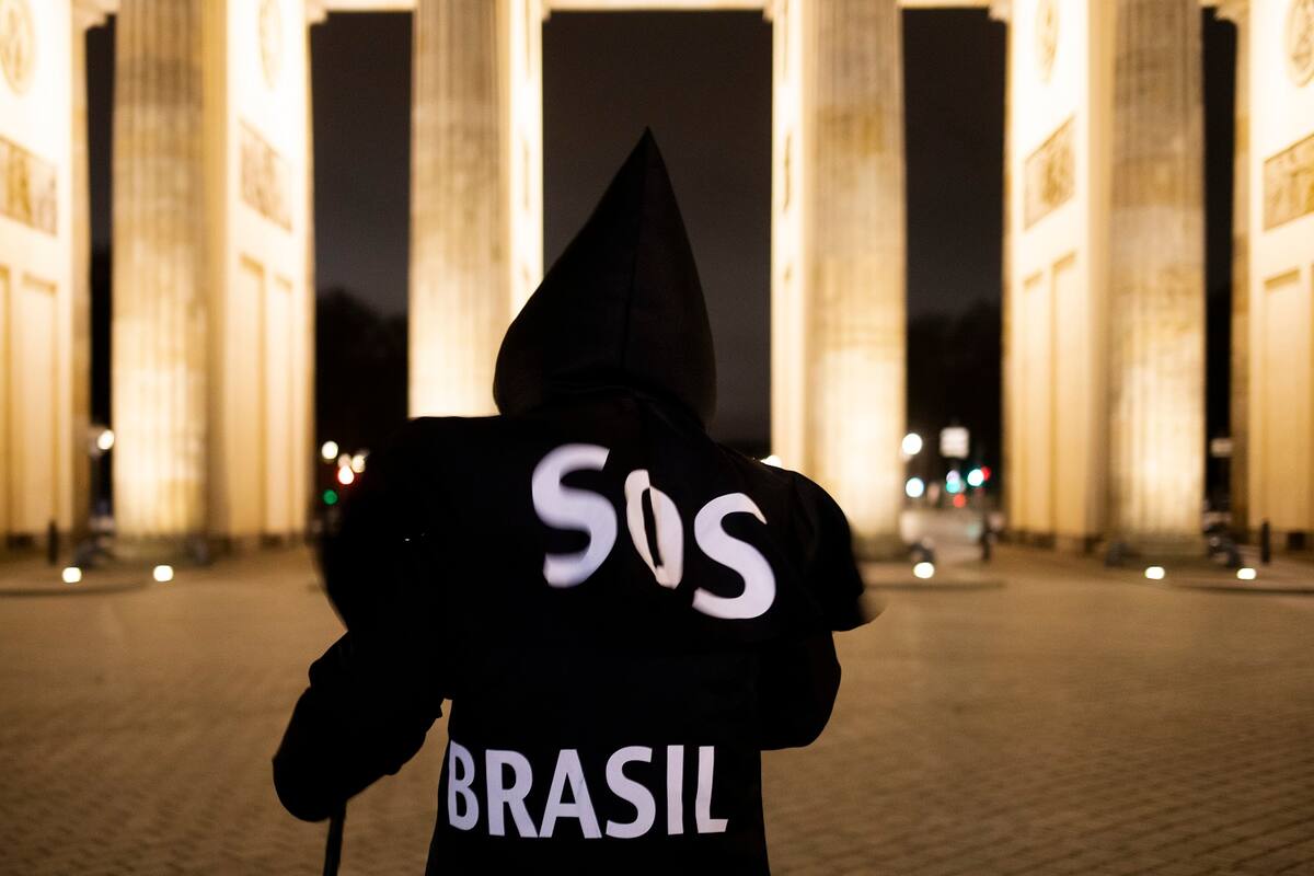 El activista y artista brasileño Rafael Puetter, disfrazado de la Parca, protesta frente a la Puerta de Brandeburgo la madrugada del miércoles 7 de abril de 2021 en Berlín. (AP Foto/Markus Schreiber)
