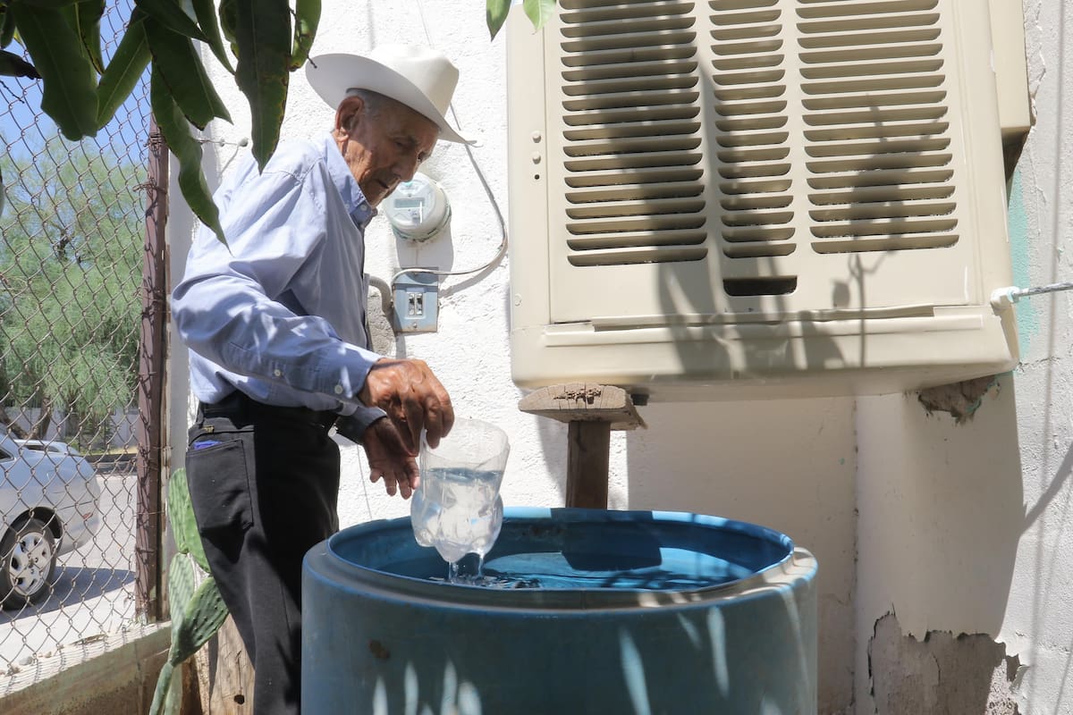 Don José Miguel Barnett, de 98 años, agarra agua de un bote para echarle al cooler, en su hogar en la colonia Primero Hermosillo.