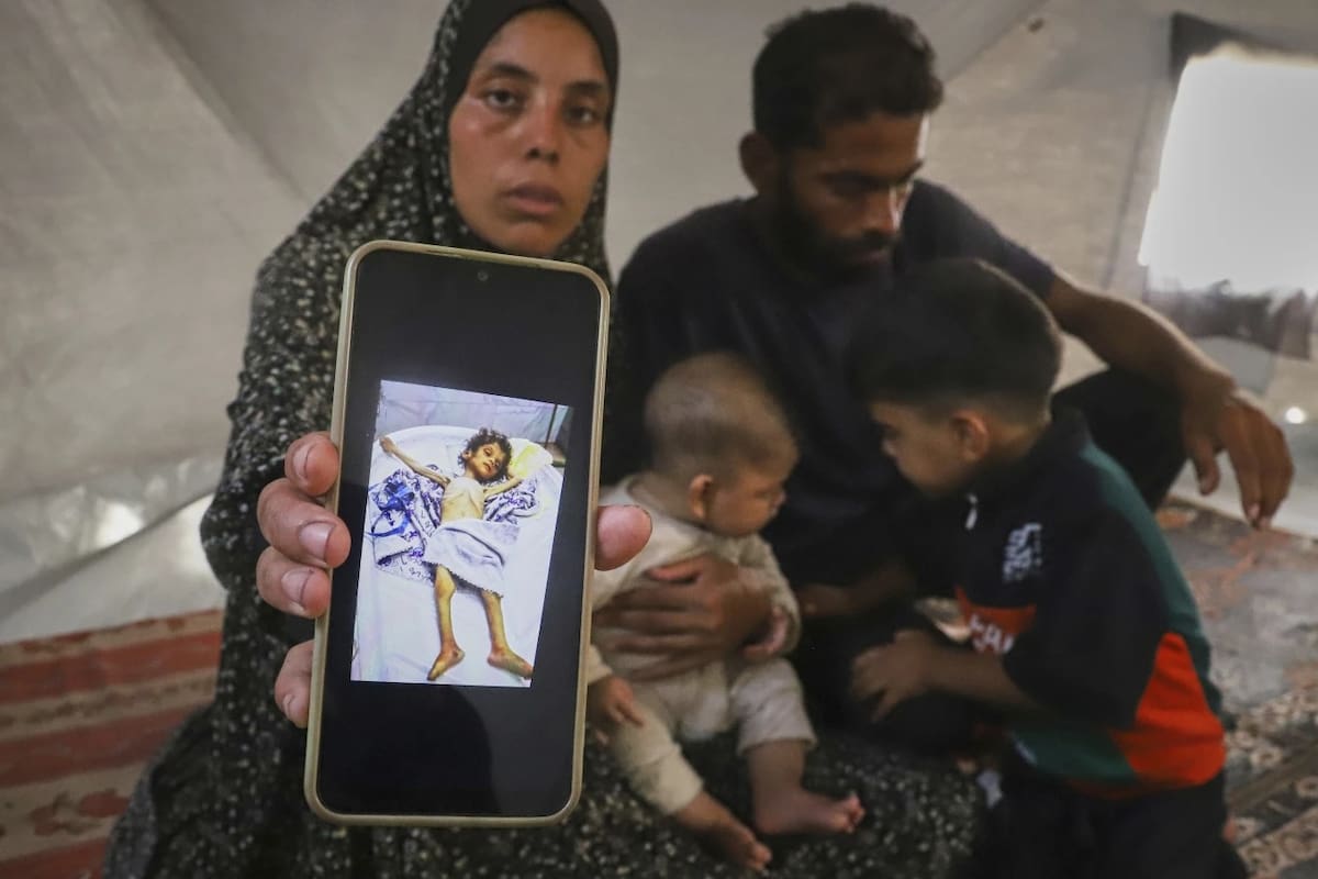 Sentada junto a su esposo, Amin, y dos de sus hijos, Fatma Mashi muestra una foto en su celular del cuerpo de su hija de dos años y medio, Ro'a, quien, según los médicos, no tenía afecciones preexistentes y murió de desnutrición severa, en su tienda de campaña en Muwasi, al sur de la Franja de Gaza, el viernes 8 de agosto de 2025. Los expertos dicen que no es inusual que un miembro de la familia esté peor que los demás. | Crédito: AP/Mariam Dagga