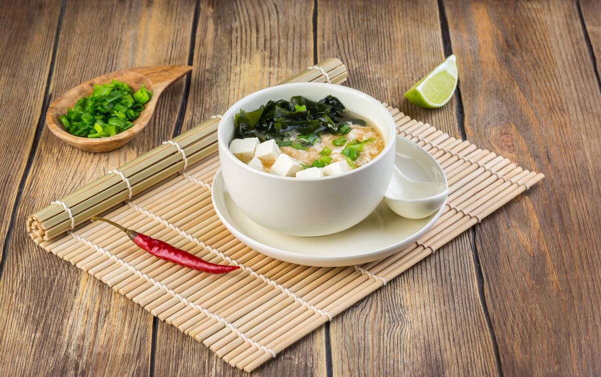 Japanese miso soup with wakame, tofu cheese and egg in a white bowl on the table covered with bamboo mat. Copy space