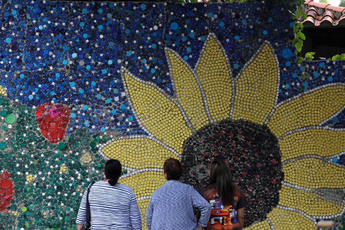 La gente observa un mural del artista venezolano Oscar Olivares en El Hatillo, en las afueras de Caracas, Venezuela, el jueves 30 de enero de 2020. Olivares, de 23 años, usó miles de tapas de botellas de plástico para crear este mural titulado "Okomural". (AP Foto / Ariana Cubillos)