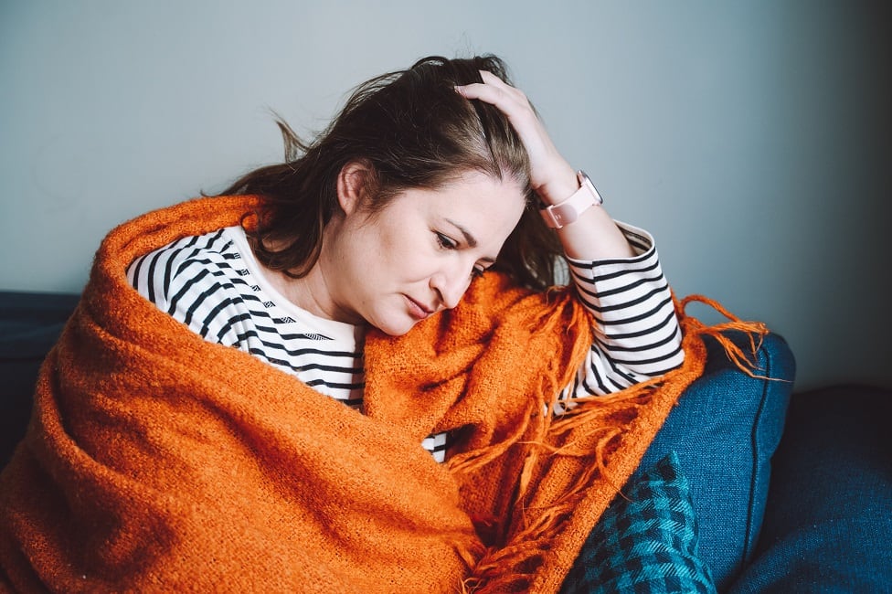 Sad woman at home alone. Woman wrapped in orange warm plaid feels sad. Early menopause, hormone therapy