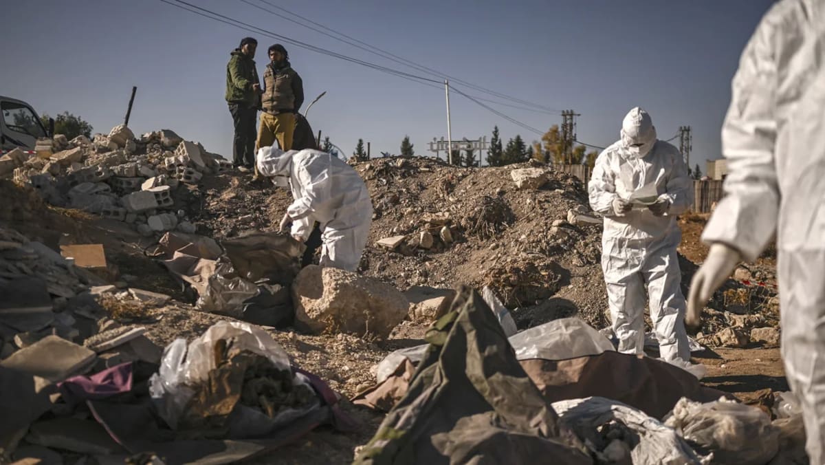 Miembros de la defensa civil de los Cascos Blancos de Siria recogen restos humanos en una fosa común descubierta en Damasco el lunes. Aris Messinis/AFP/Getty Images