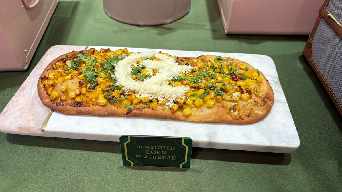 Un pan con elote con una montaña de queso que da forma al logo de Oz.